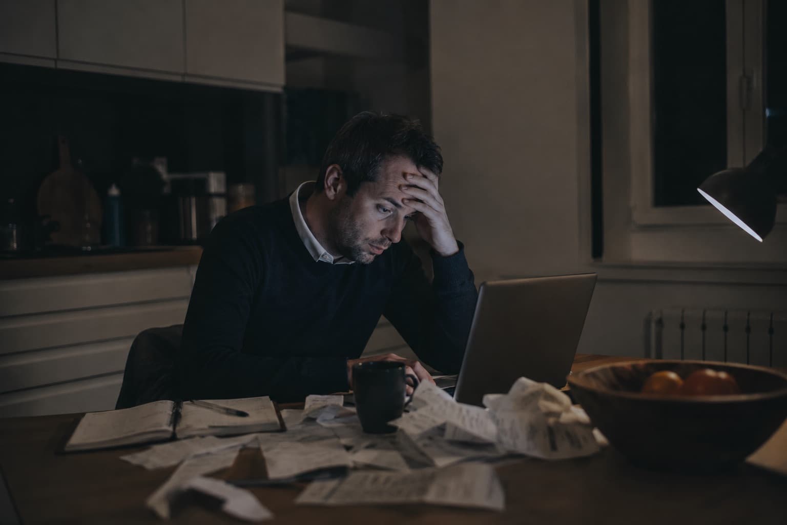 Un commercial ressaisit ses notes dans son CRM tard le soir, à la table de la cuisine